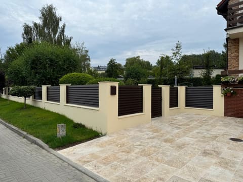 Nowoczesne ogrodzenie z ciemnych paneli i jasna kostka brukowa wykonane przez DBF